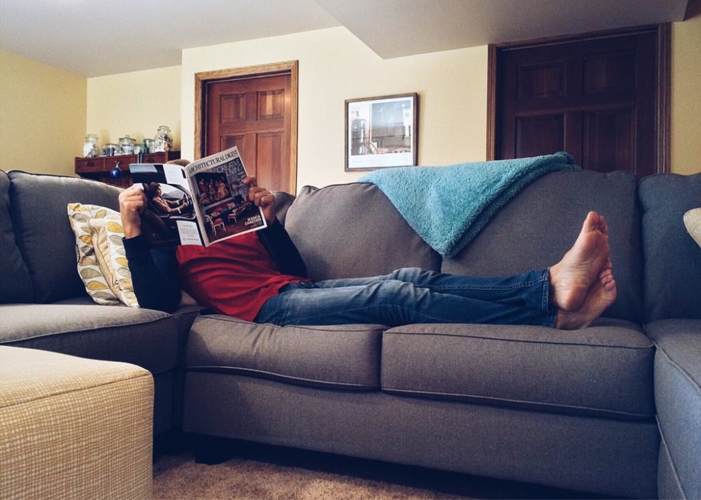 Guy reading a newspaper while laying on couch