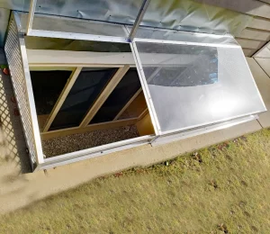 Large super-slant cover on a concrete well. The cover has an egress escape hatch which is pushed open.