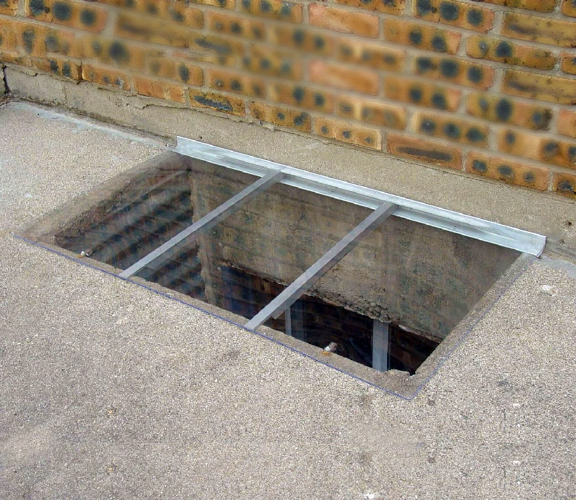 Ground-level window well with a sloped cover. The overlap is minimal. Size of cover: 46 x 26